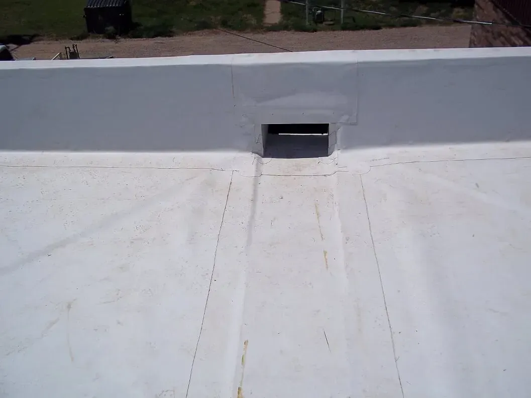 White roof membrane with a gray parapet wall and small rectangular vent opening.