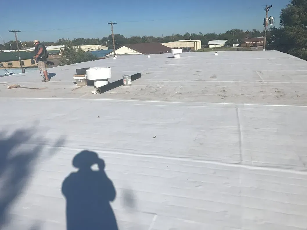 Flat white rooftop with vents under a clear blue sky, with a person’s shadow in the foreground.