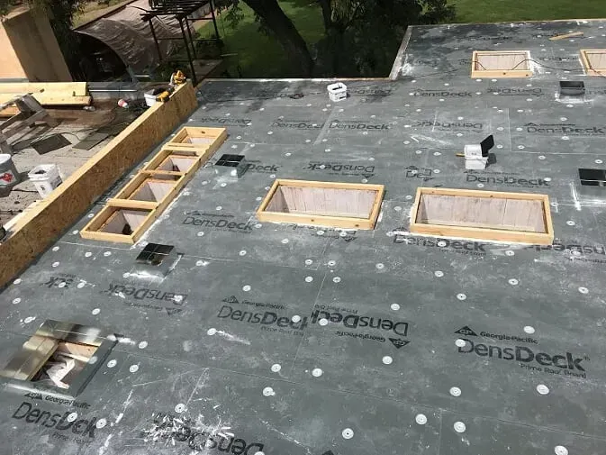 Roof under construction with black waterproofing membrane and several rectangular skylight openings