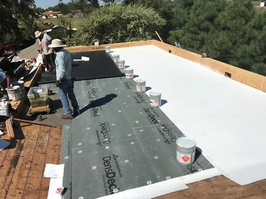 Workers installing roofing on a flat roof, with white membrane and gray underlayment in progress.
