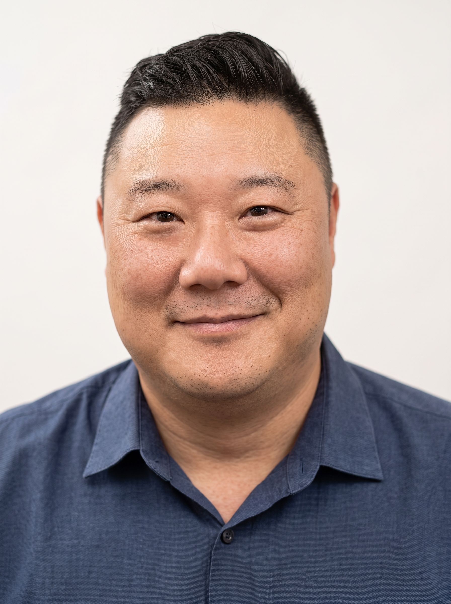 Smiling man in a blue collared shirt against a plain light background
