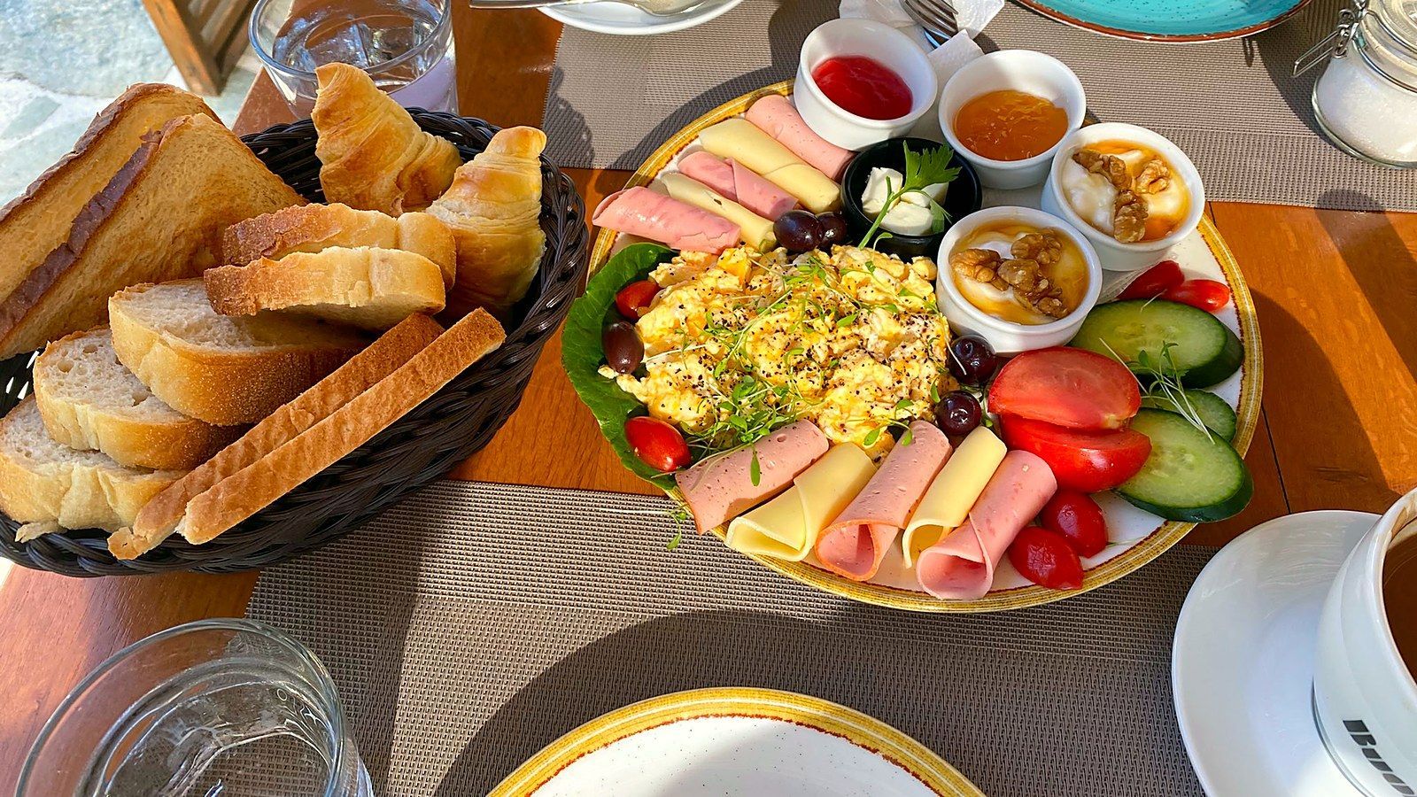 Full breakfast plate with scrambled eggs, cheese, ham, Greek yogurt with honey and walnuts, and a bread basket with croissants at Villa Karina
