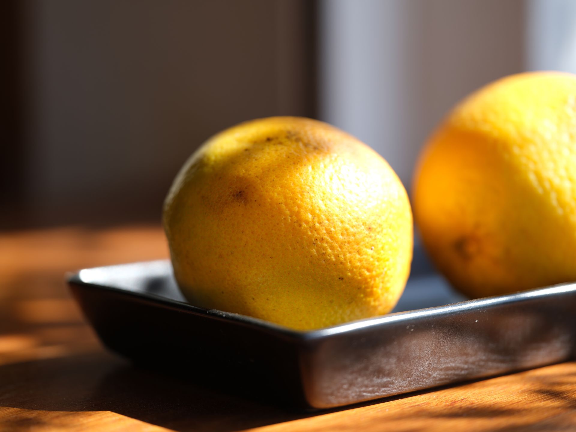 Two lemons sit on a black tray on a wooden table