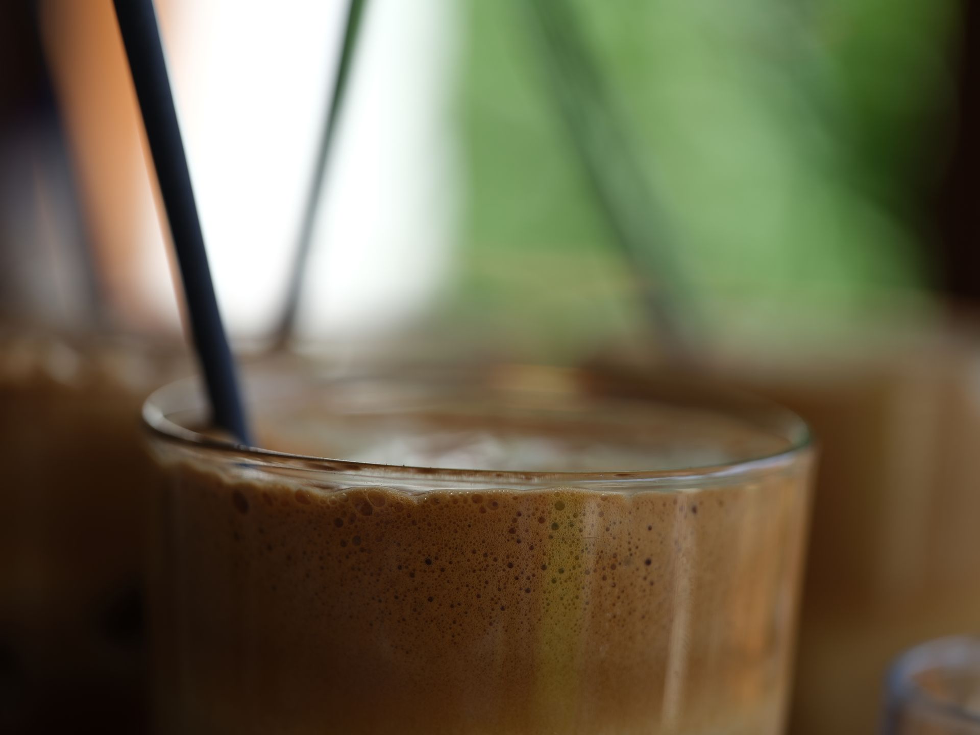 A close up of a glass of coffee with a straw in it.
