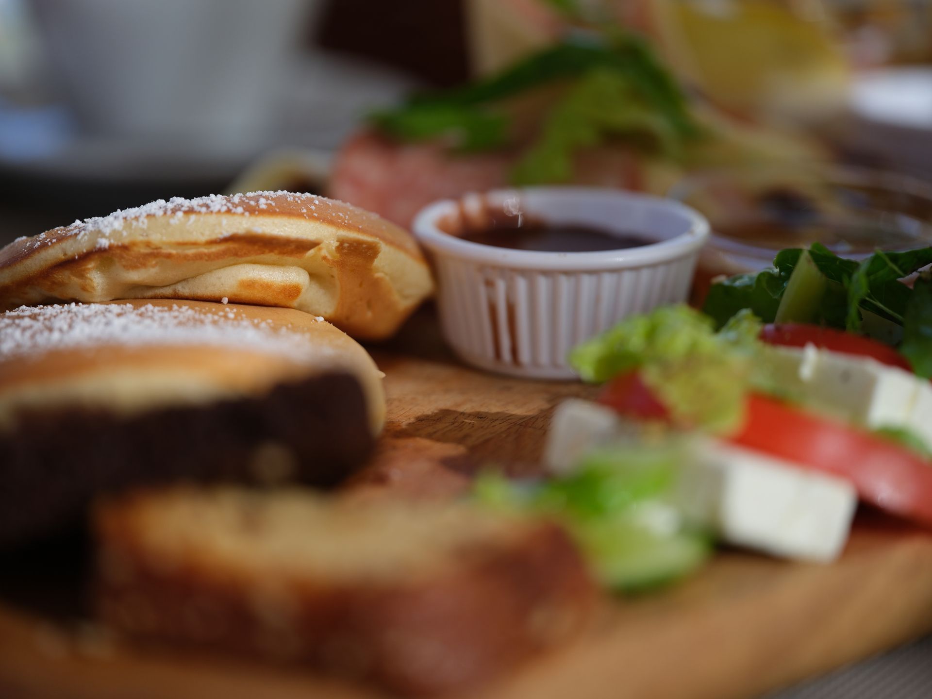 A wooden cutting board topped with sandwiches and a small bowl of sauce.