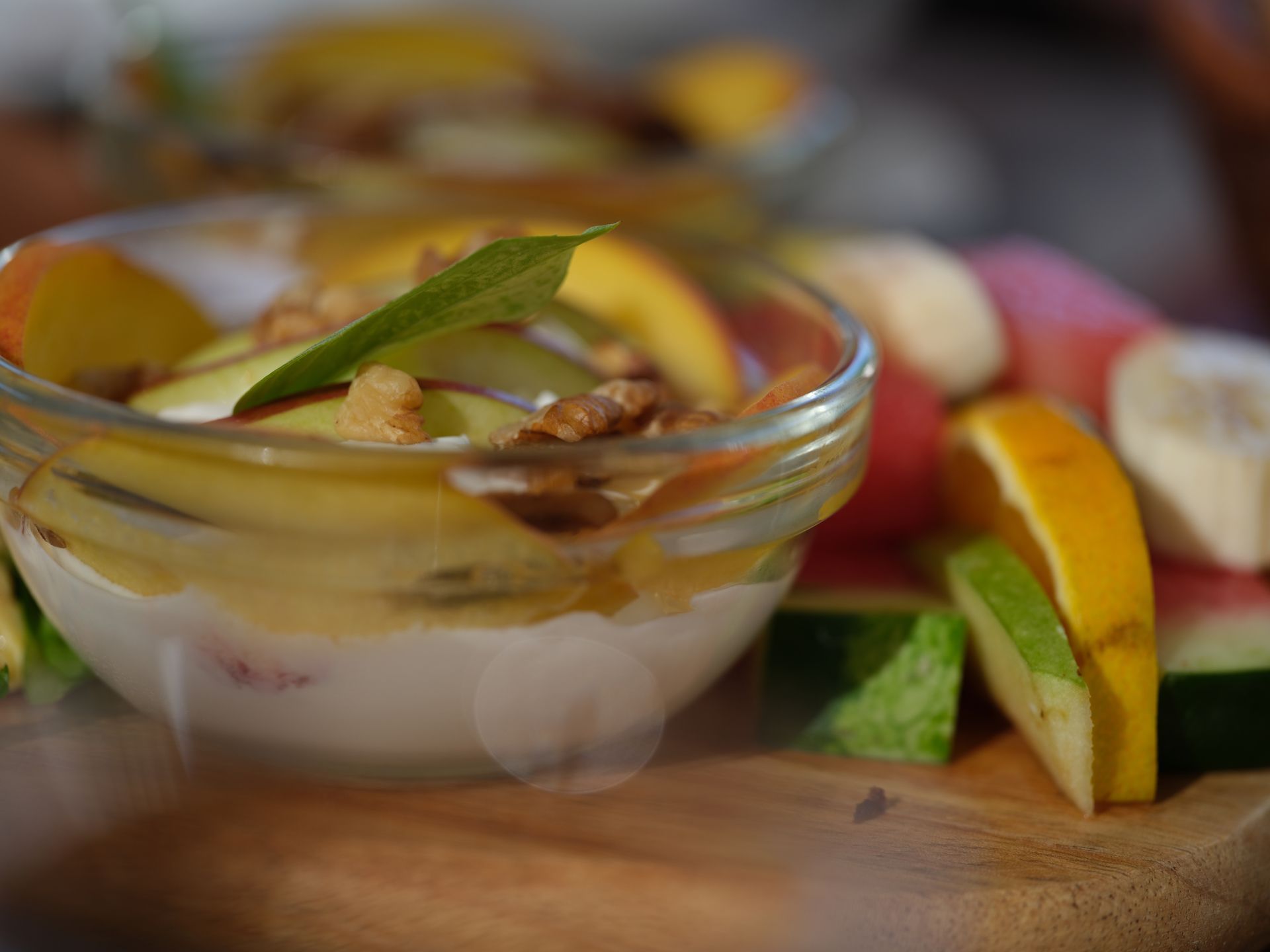A bowl of fruit and yogurt on a wooden cutting board.
