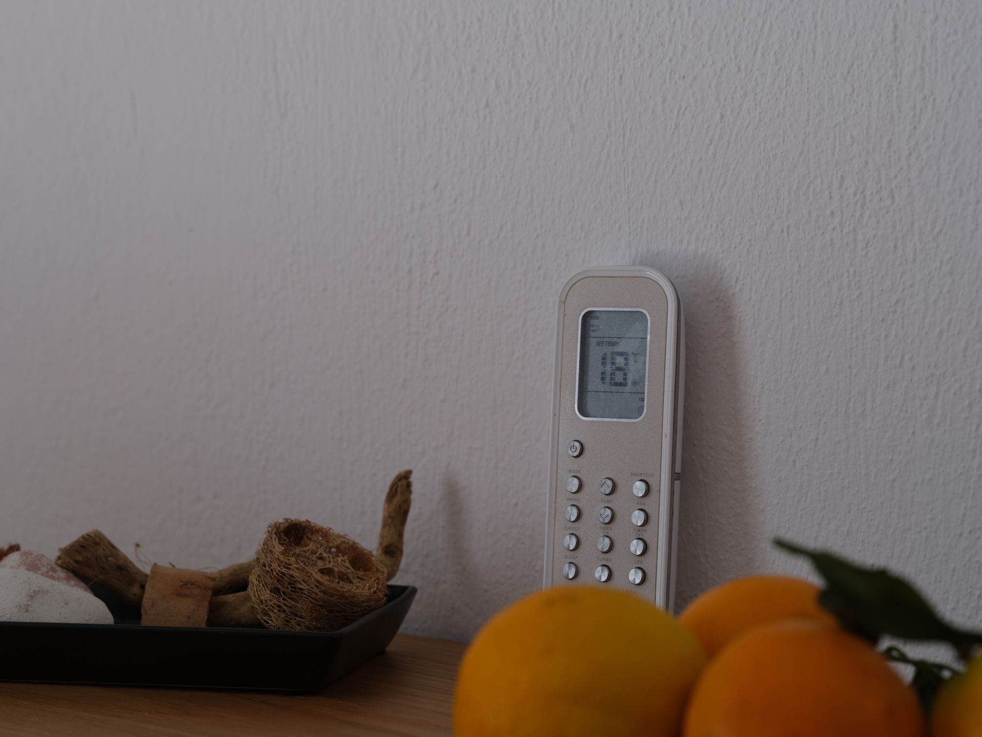 A remote control is sitting on a table next to a tray of oranges.