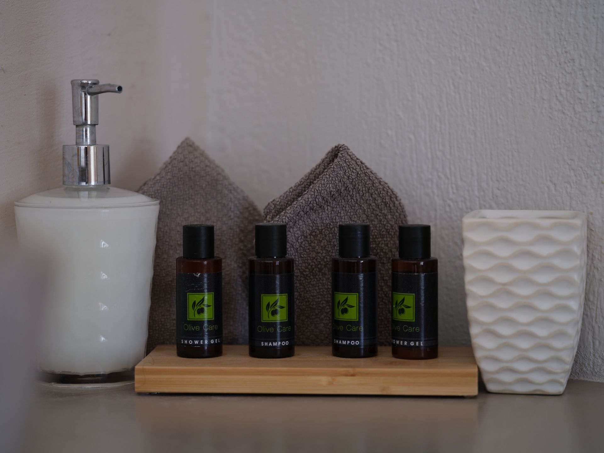 Four bottles of lotion are sitting on a wooden tray next to a soap dispenser.