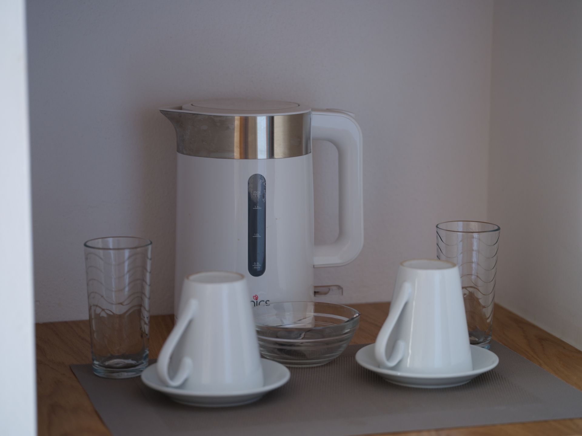A white kettle sits on a table next to two cups and glasses