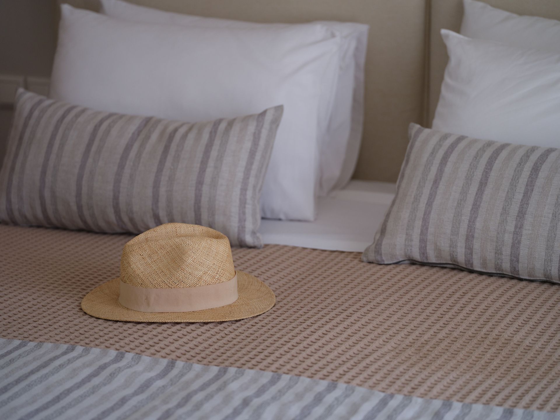A straw hat is sitting on a bed with striped pillows.