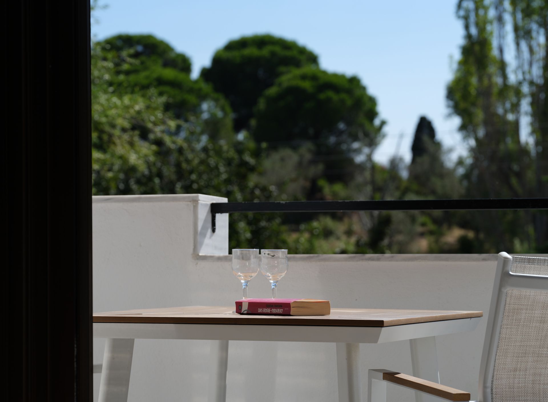 A table with two wine glasses and a book on it on a balcony.