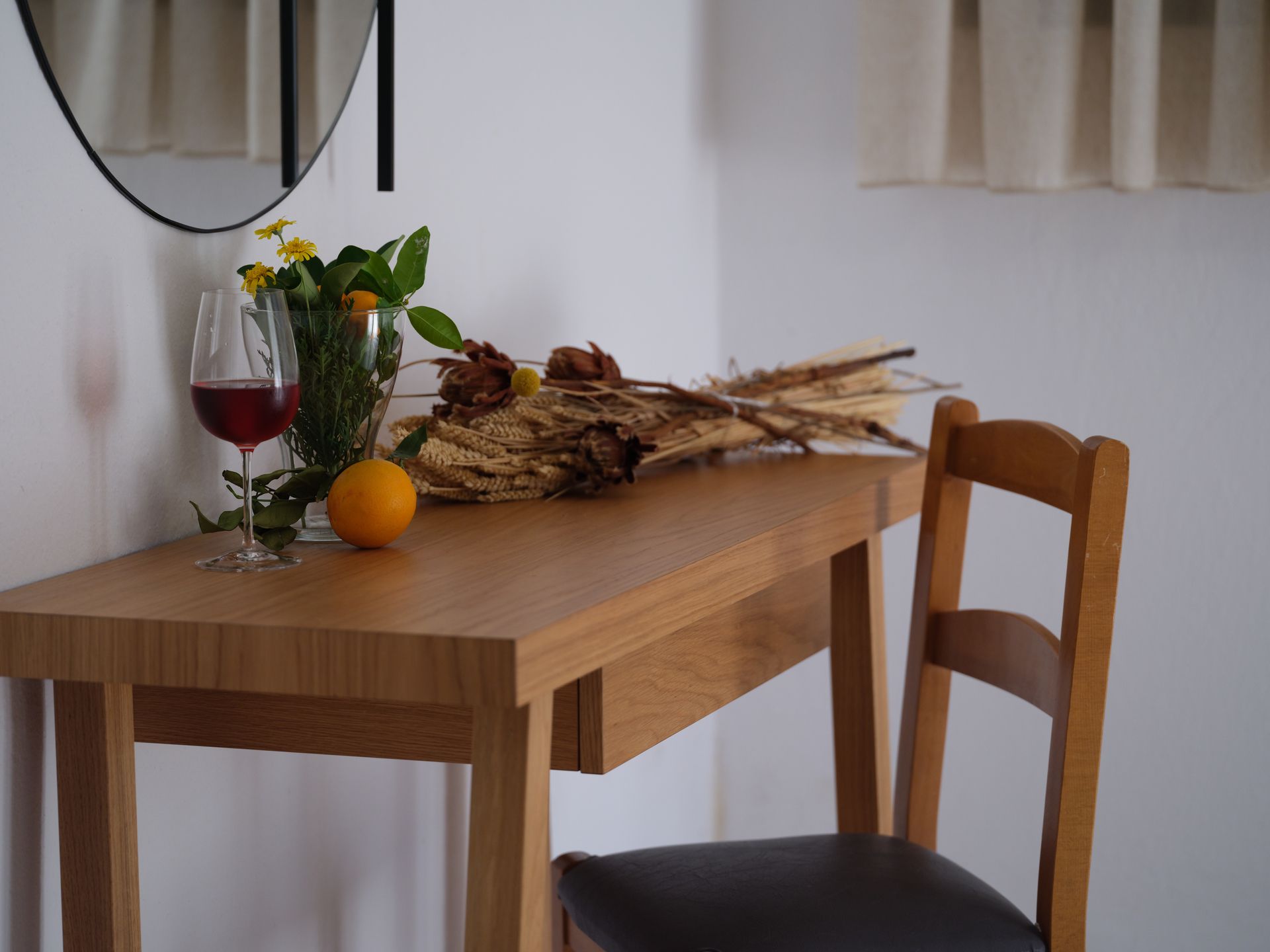 A wooden table with a vase of flowers and a glass of wine on it