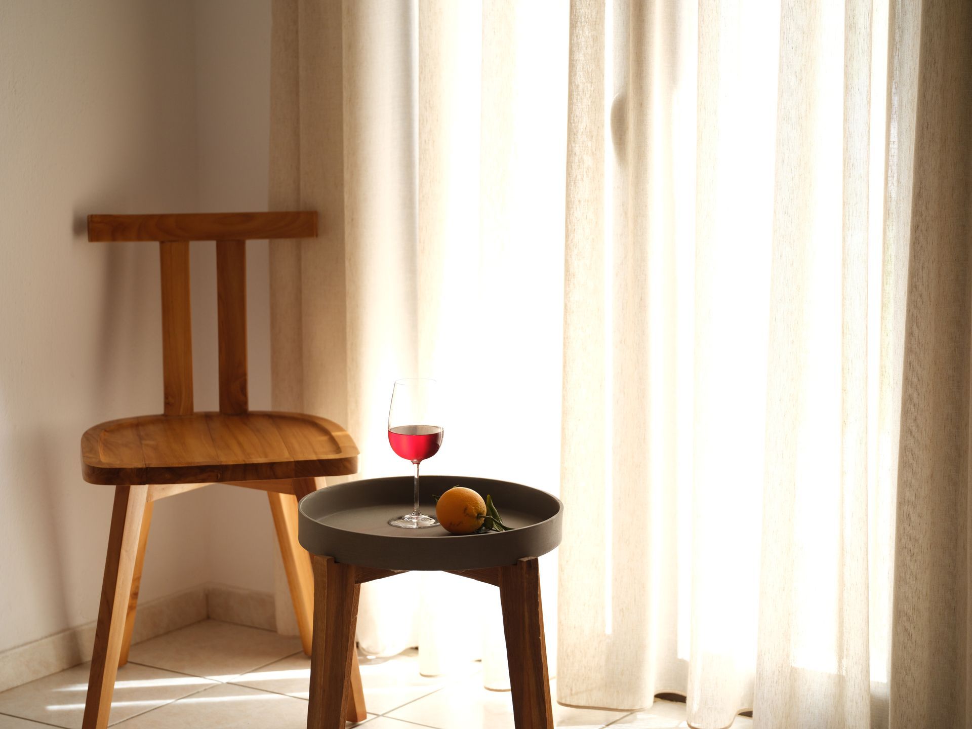 A wooden chair is sitting next to a table with a glass of wine and an orange on it.