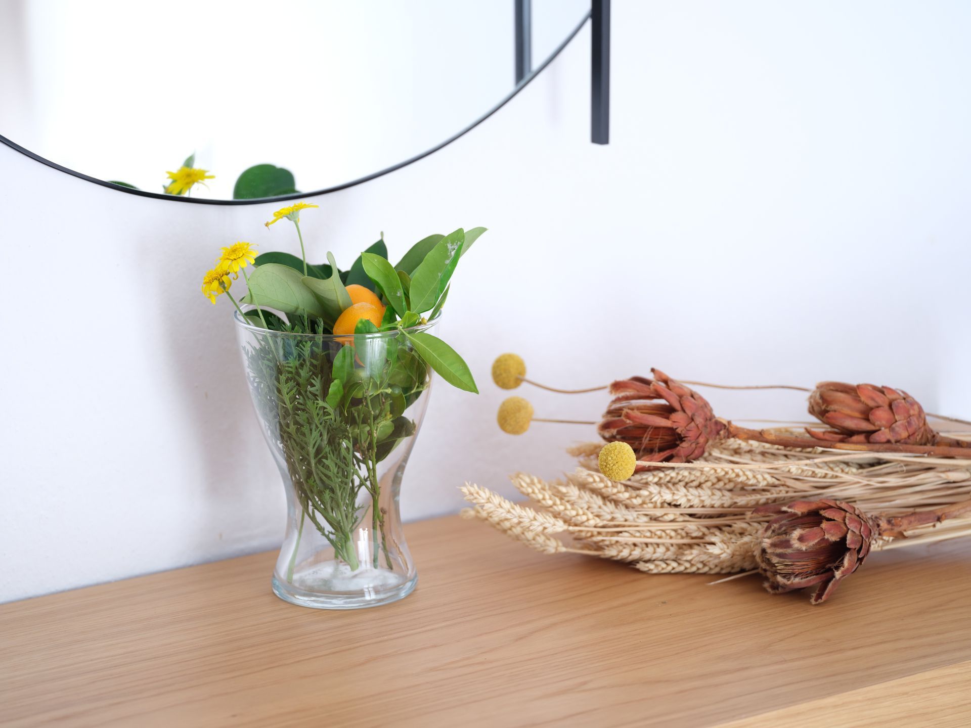 A vase filled with flowers sits on a wooden table next to a mirror.
