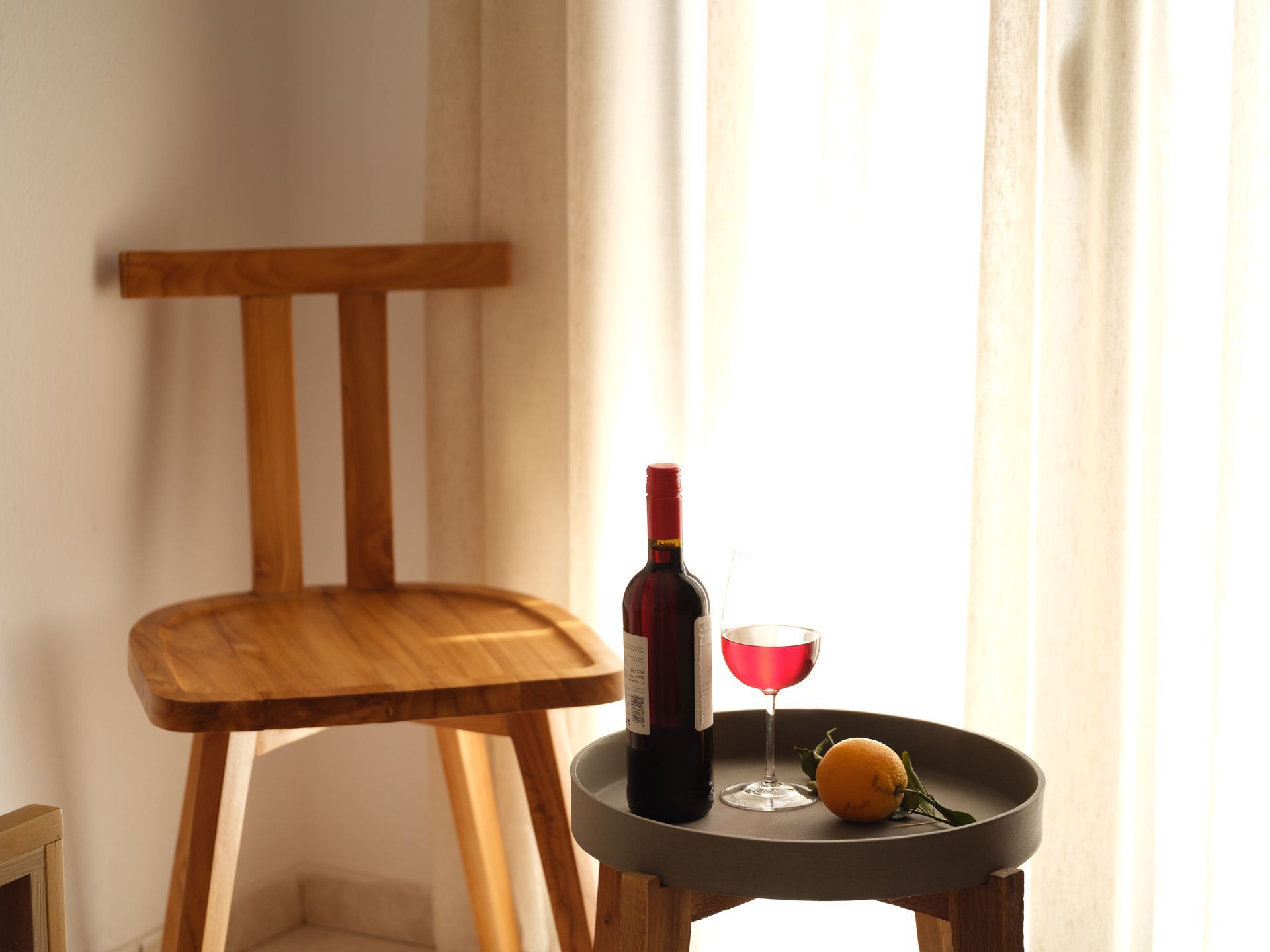 A wooden chair is sitting next to a table with a bottle of wine and a glass of wine on it.