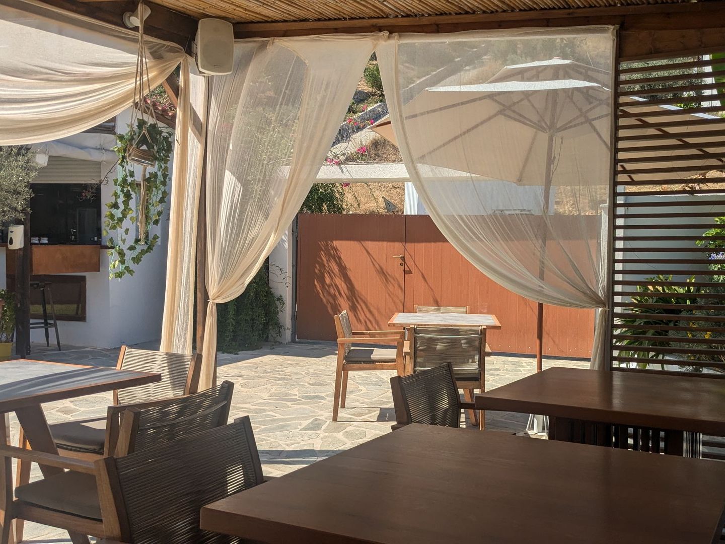 A patio with tables , chairs and umbrellas under a canopy.