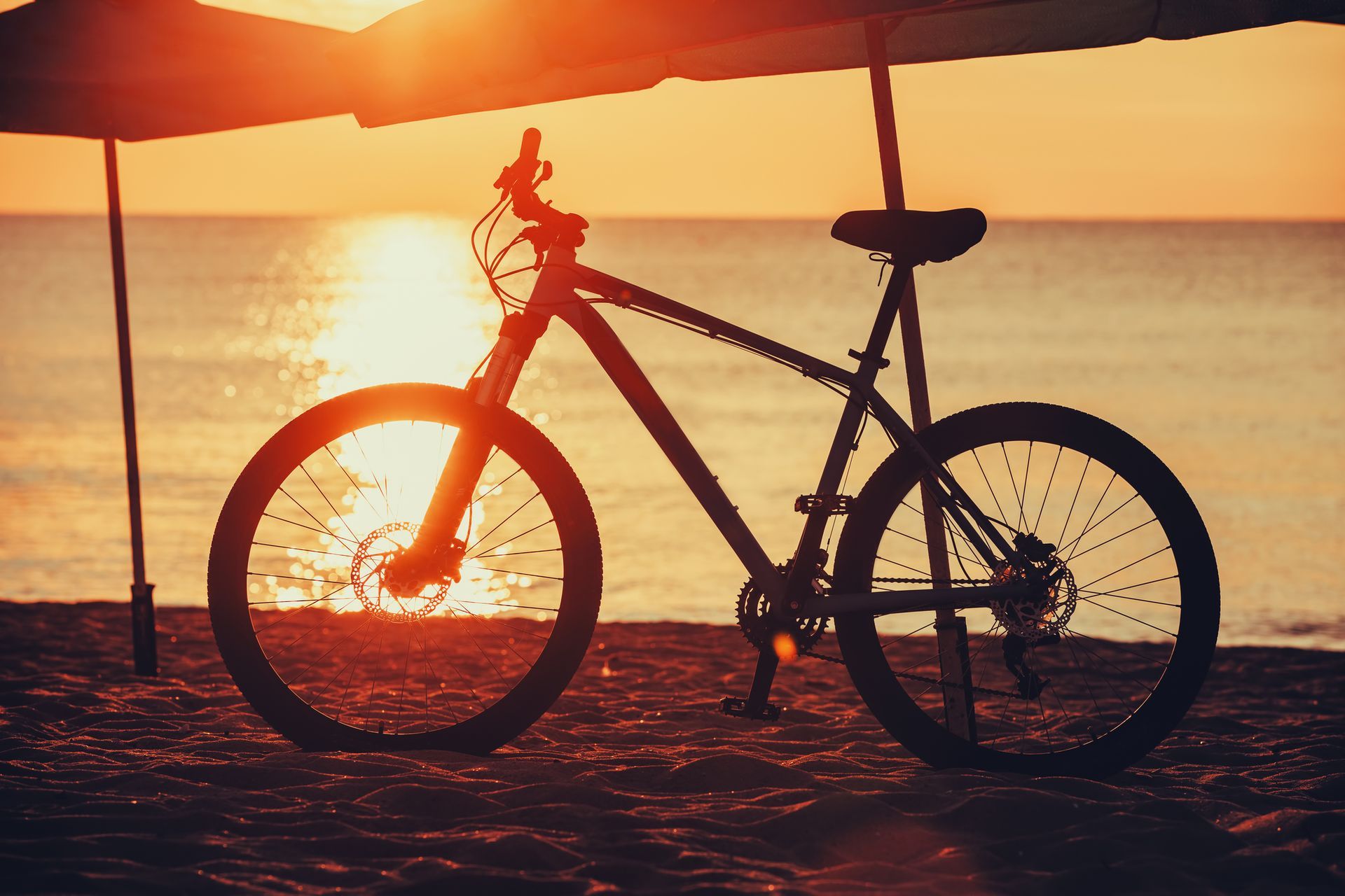 A bicycle is parked on the beach at sunset.
