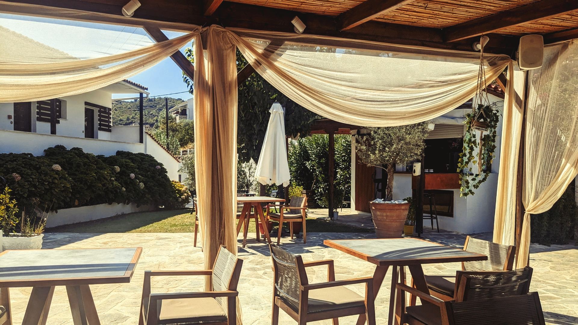 A patio with tables and chairs under a canopy with a white umbrella.
