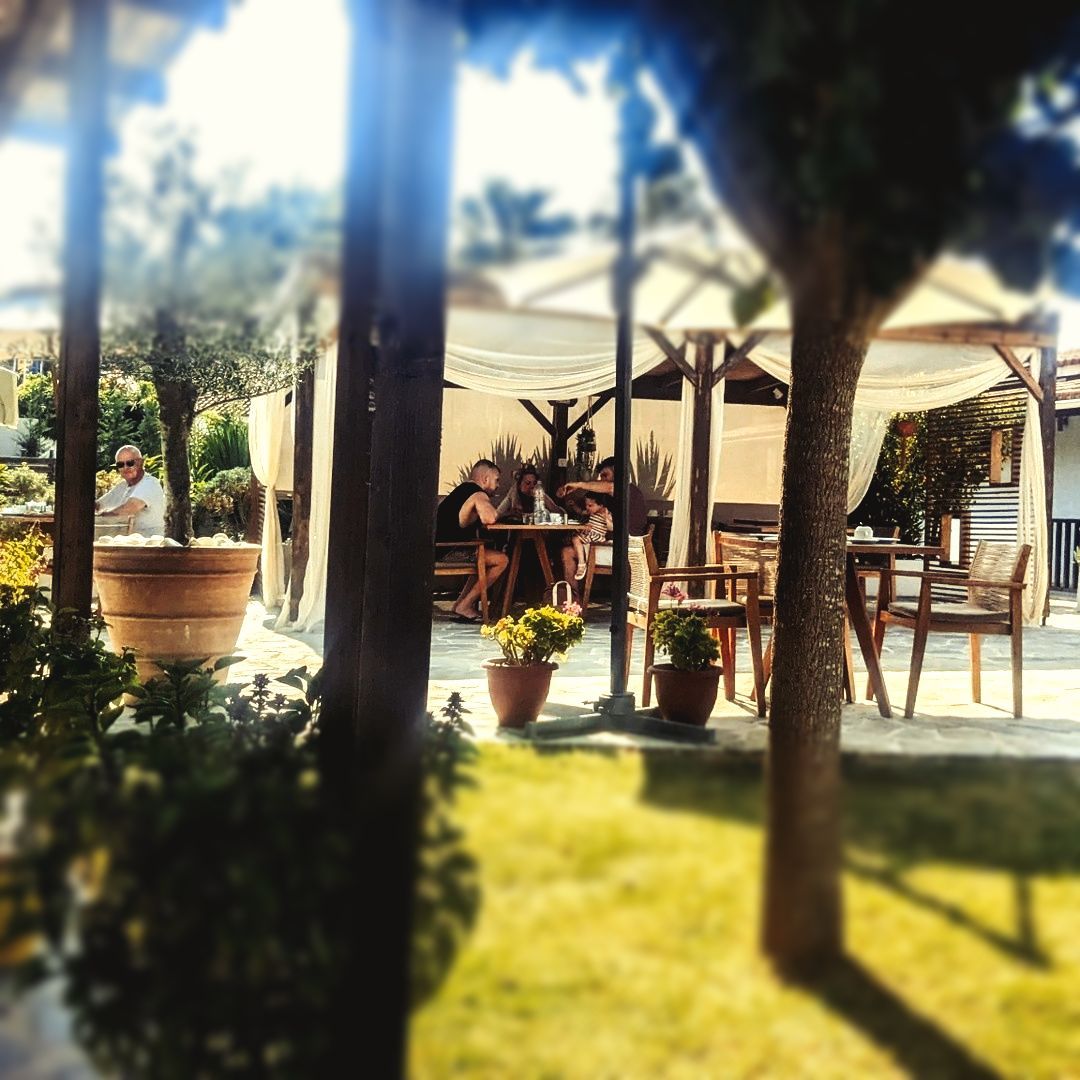 A group of people are sitting at tables under an umbrella