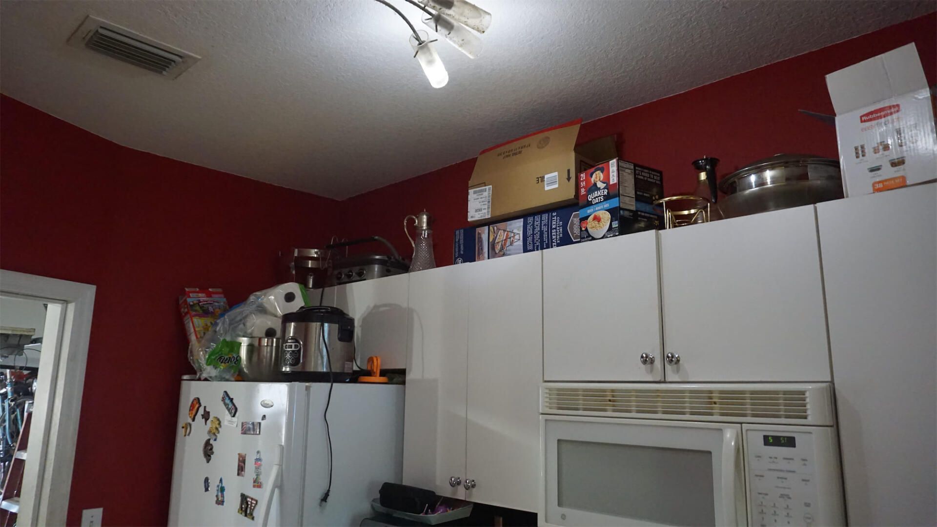 a kitchen with red walls , white cabinets , a microwave and a refrigerator .