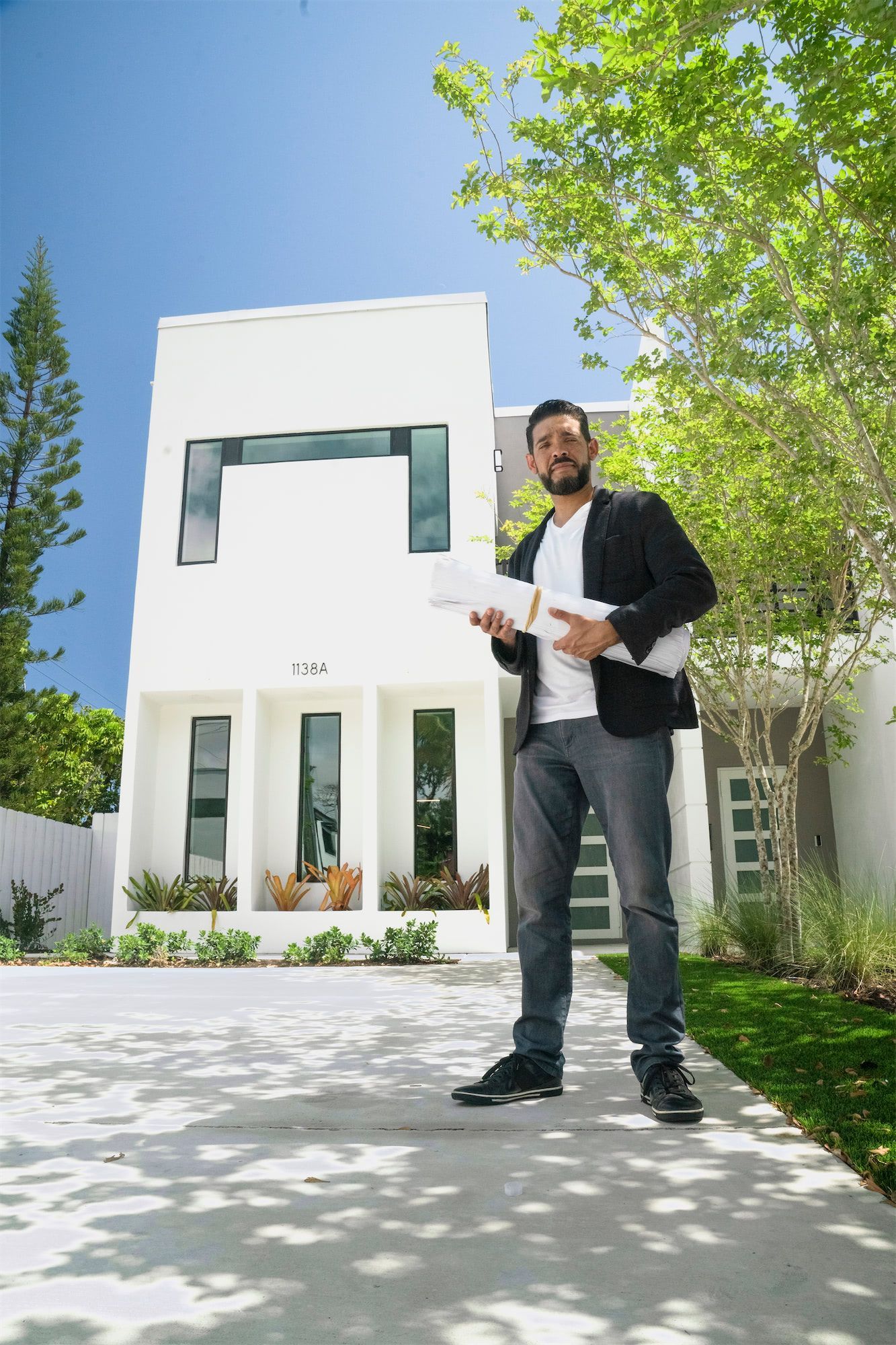 a man is standing in front of a white house holding a blueprint .