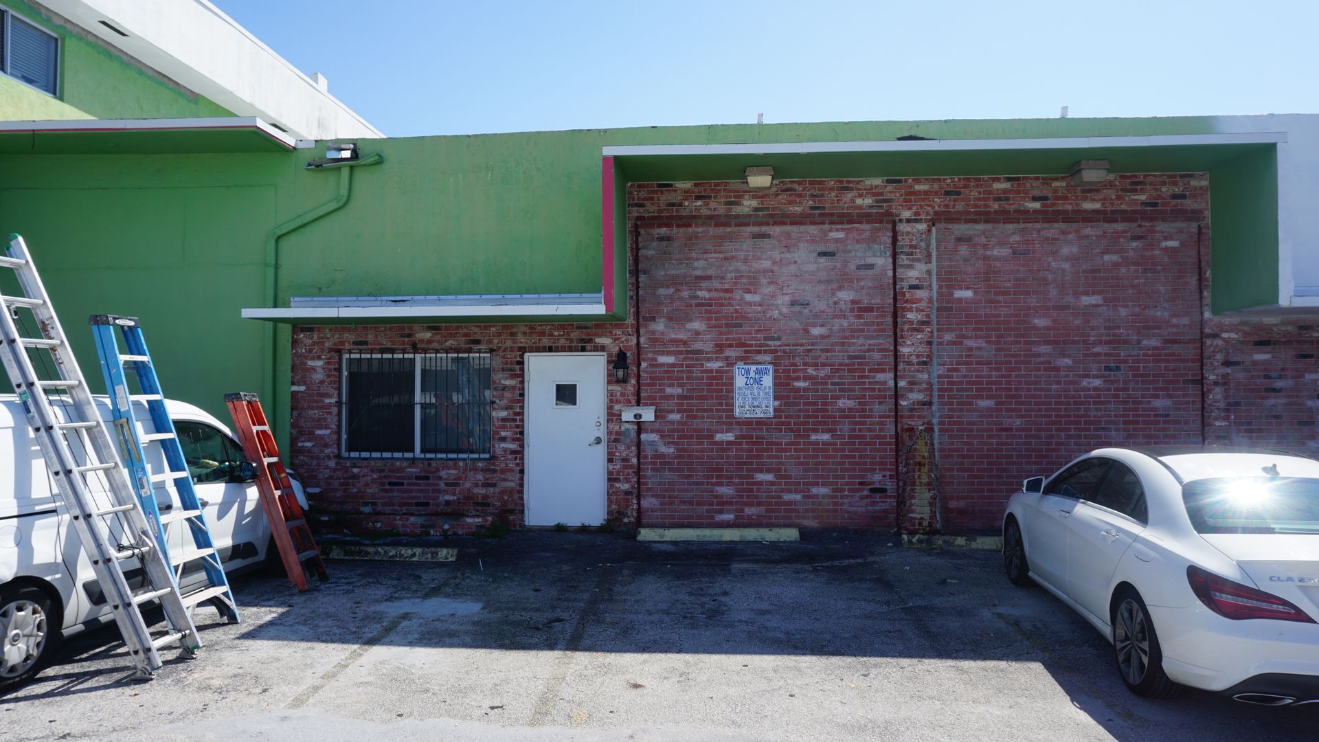 A white car is parked in front of a green building with a partial brick wall.