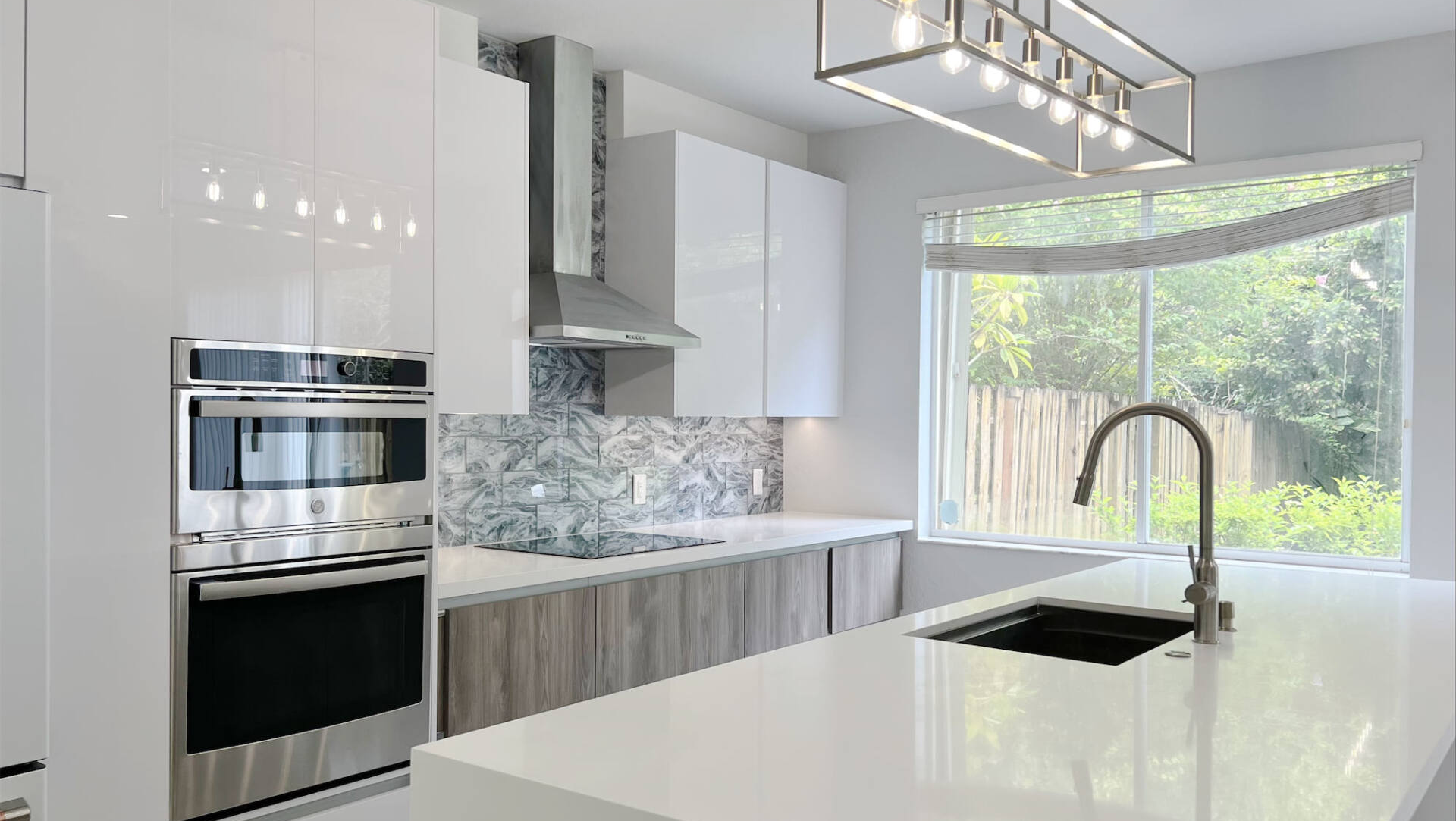 a kitchen with white cabinets , stainless steel appliances , a sink , and a large window .