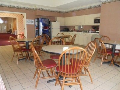 A dining area with round tables, wooden chairs, a kitchen, and a vending machine.