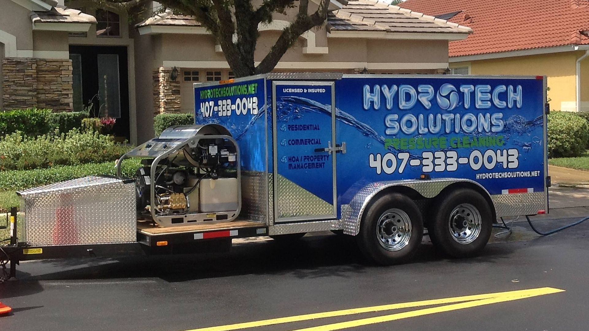 Hydrotech Solutions trailer parked on a street in front of a house, with blue and silver equipment branding.