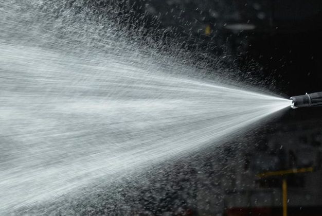 A close up of a high pressure washer spraying water on a black background.