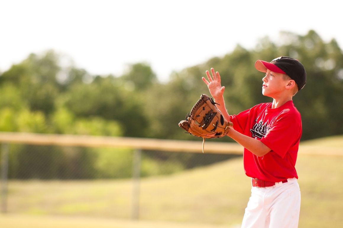 A person wearing a hat and orange shirt, holding a baseball bat on their shoulder on a baseball field.