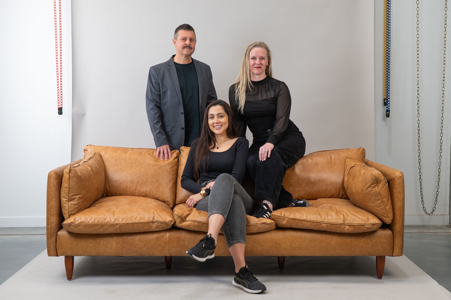 Three people pose on a brown leather couch against a white wall — Gracia Building Design In Kiama, NSW