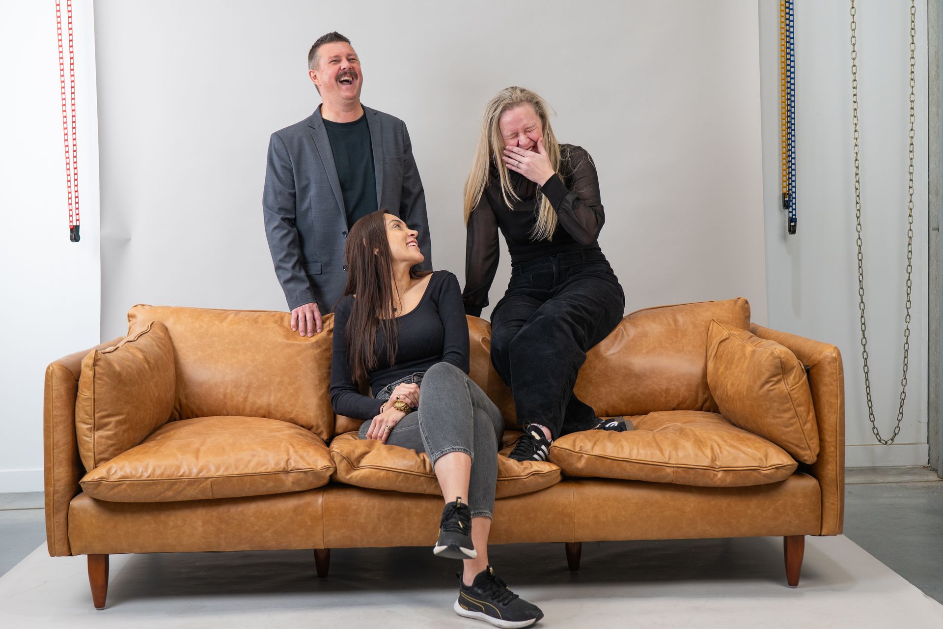 Three Laughing People on a Brown Leather Couch — Gracia Building Design In Kiama, NSW