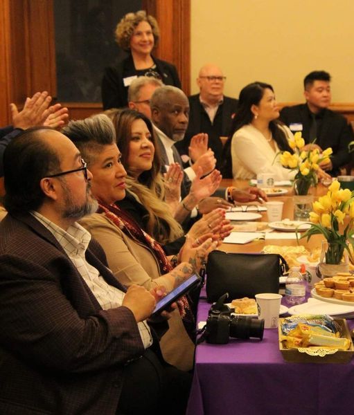 Members of the Iowa Unity Coalition and lawmakers sit around a table applauding at the 3rd Annual Legislative Breakfast.