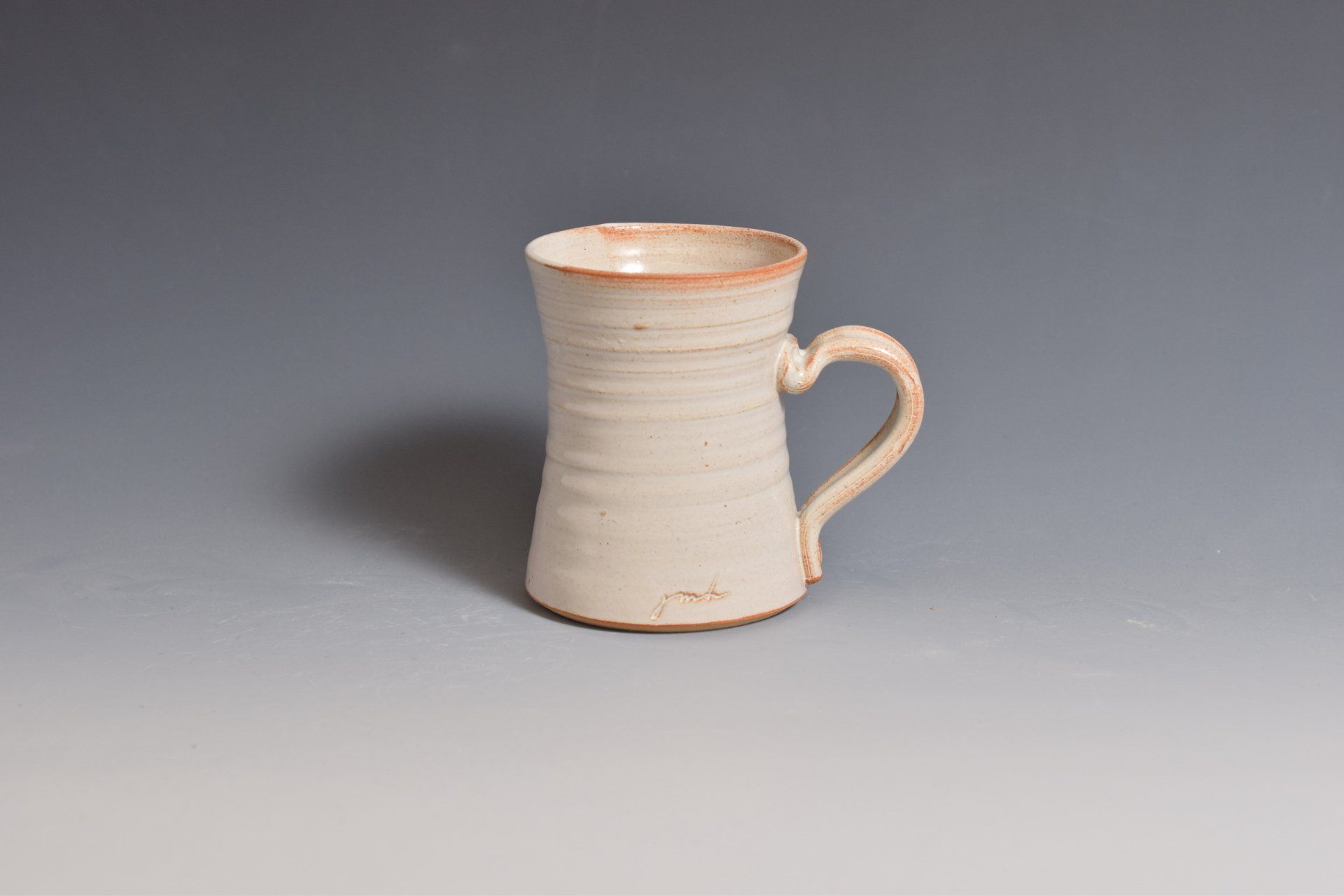 a white mug with a heart shaped handle is sitting on a table .