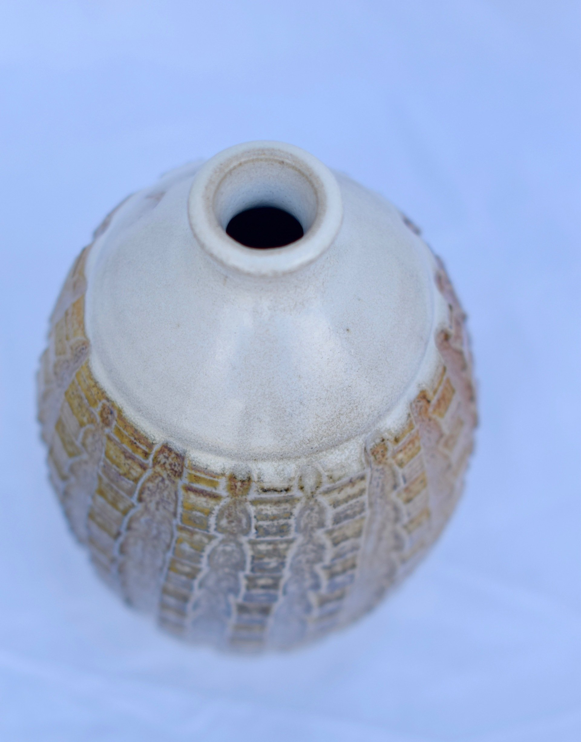 Ceramic vase with textured, light brown surface and white top. Dark opening.