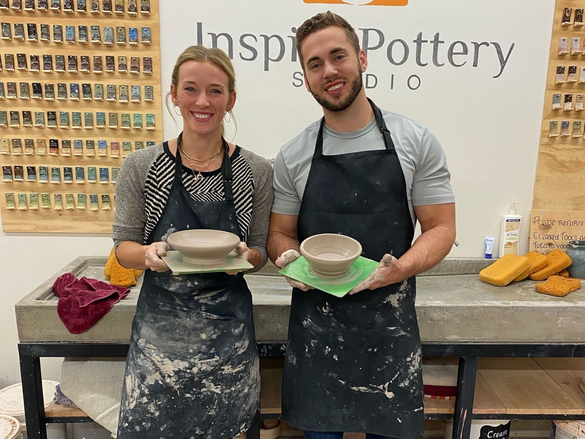 A man and a woman are holding bowls in front of a pottery studio.