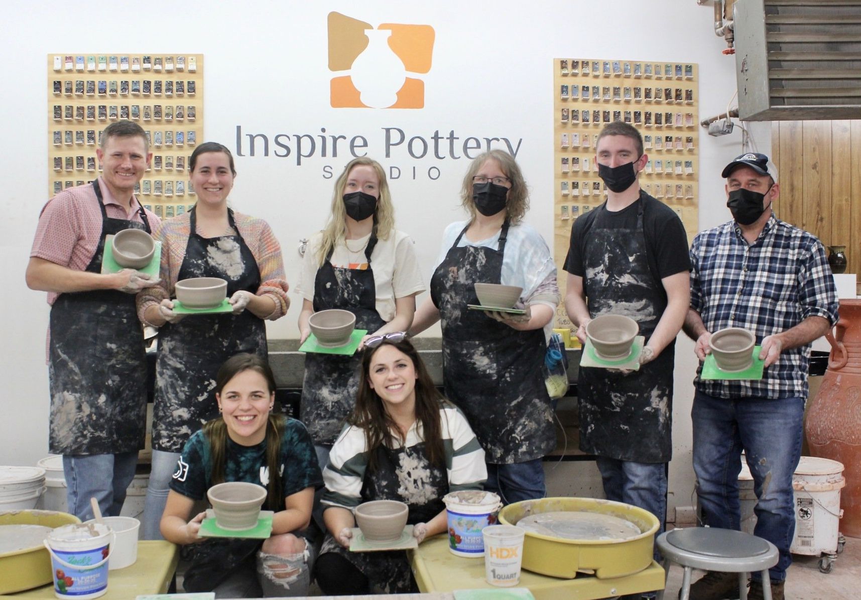 Group of people at Inspire Pottery Studio holding pottery bowls, some wearing masks.