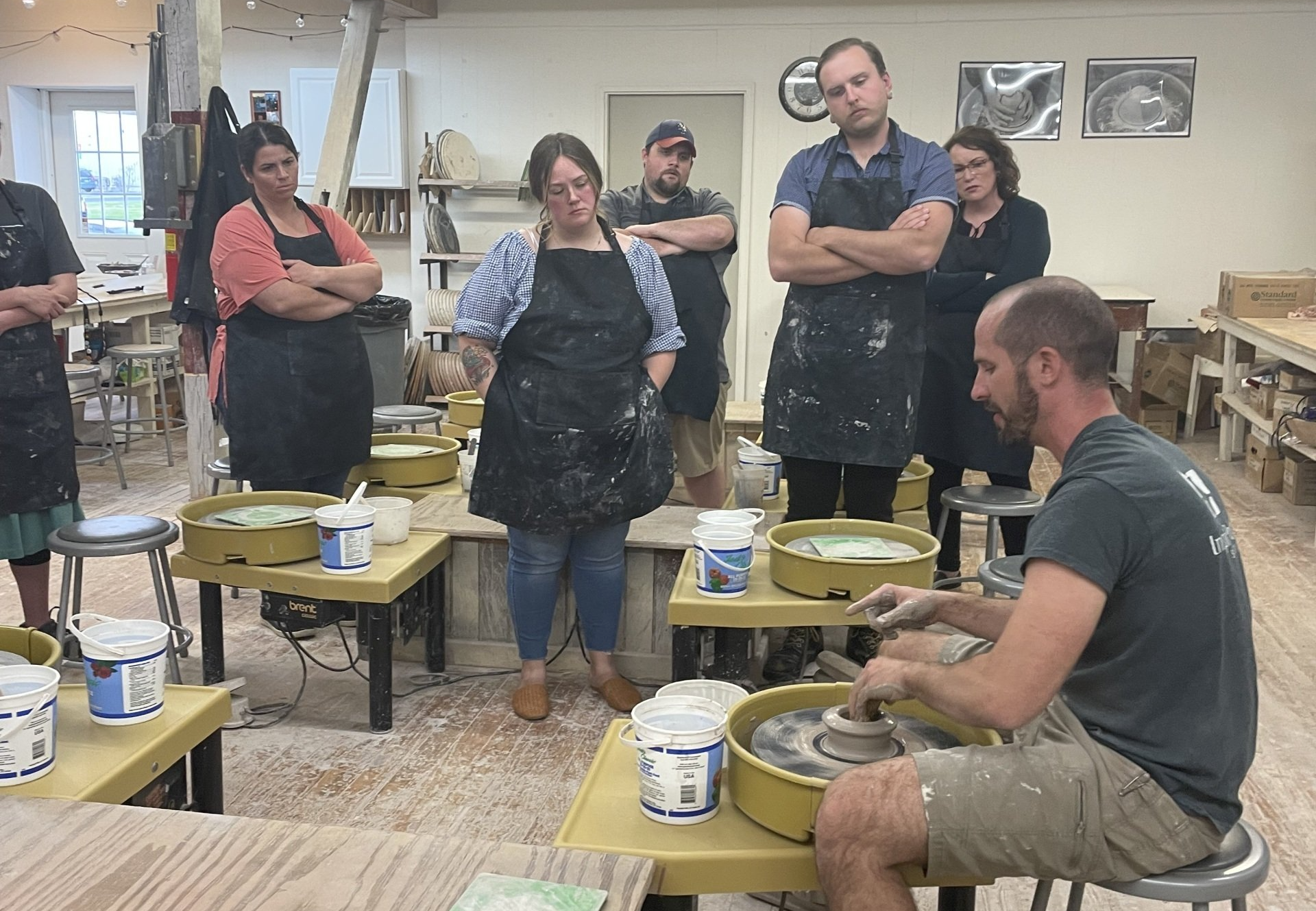 A group of people are standing around a pottery wheel in a workshop.