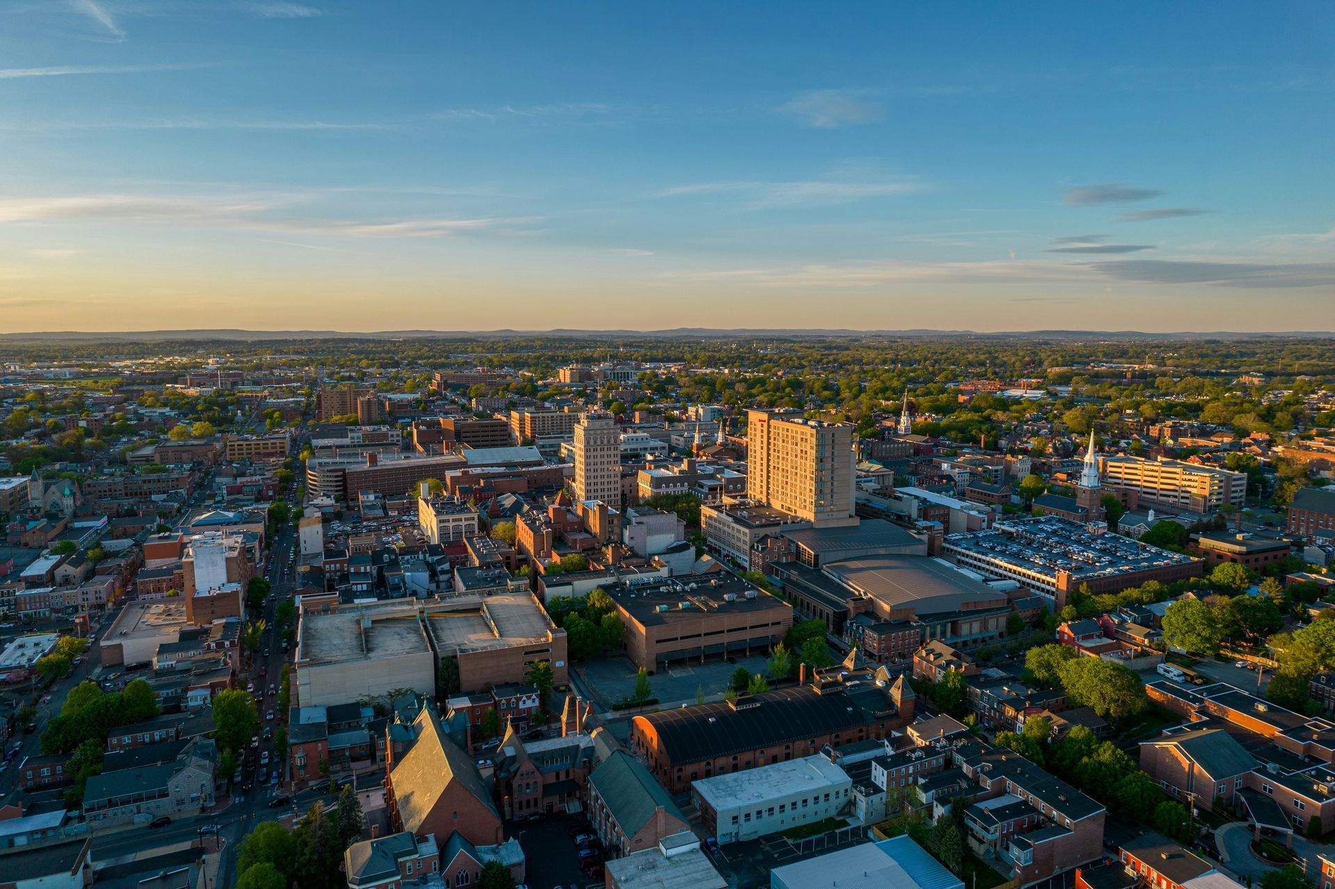 Aerial view of a city with buildings and trees under a blue and gold sky.