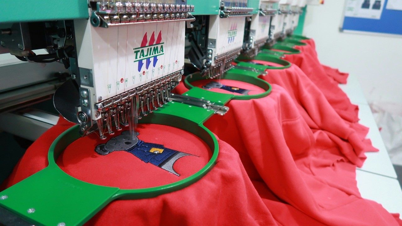 Sewing machine stitching a red baseball cap with black logo detail