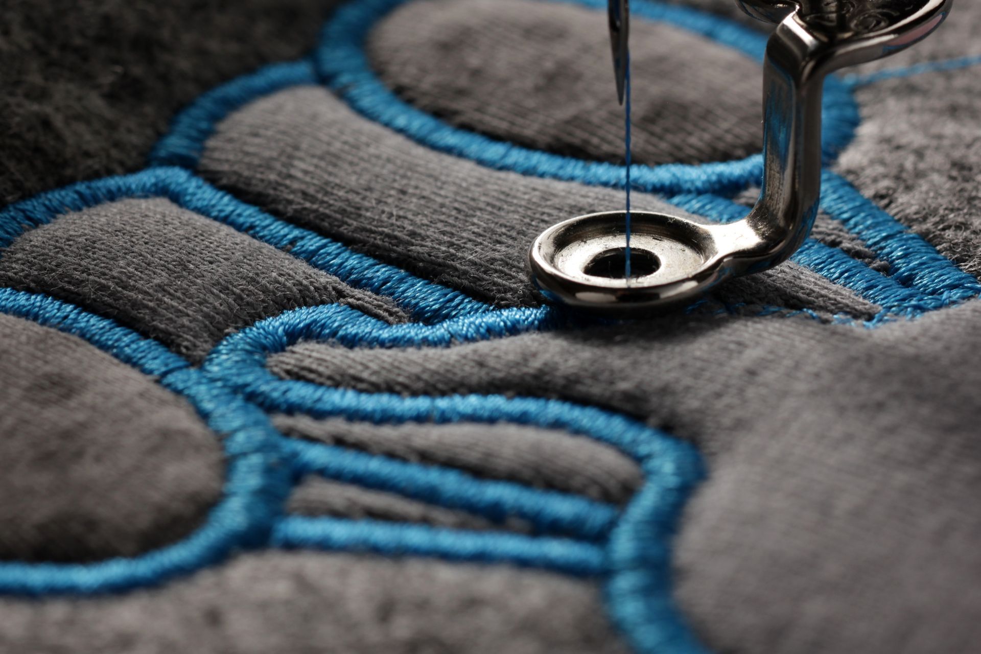 Close-up of a sewing machine stitching blue thread on dark gray fabric