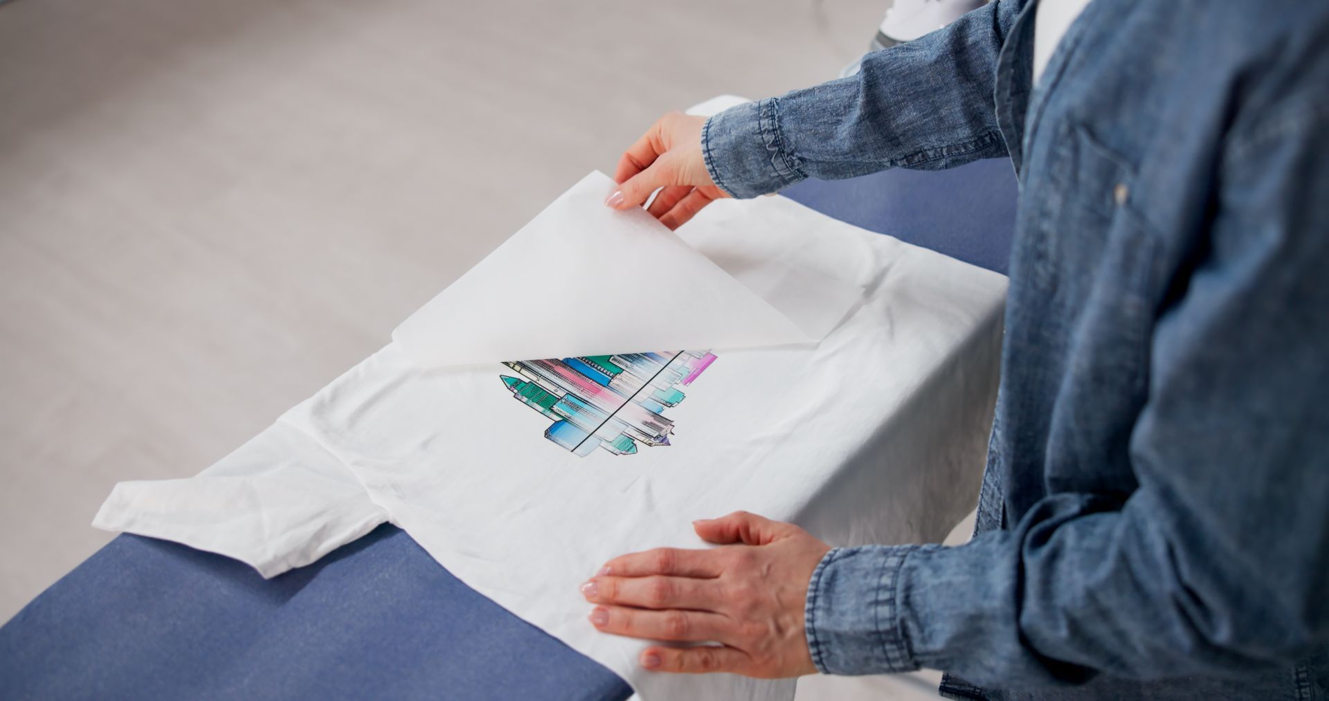 Person folding a white T-shirt with a colorful graphic on a bed