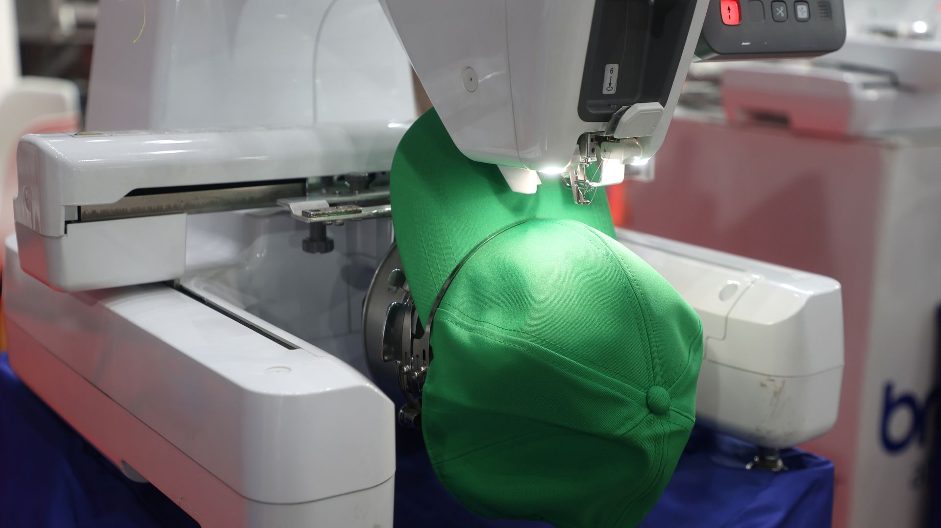 Green cap being embroidered by a machine in a sewing workshop