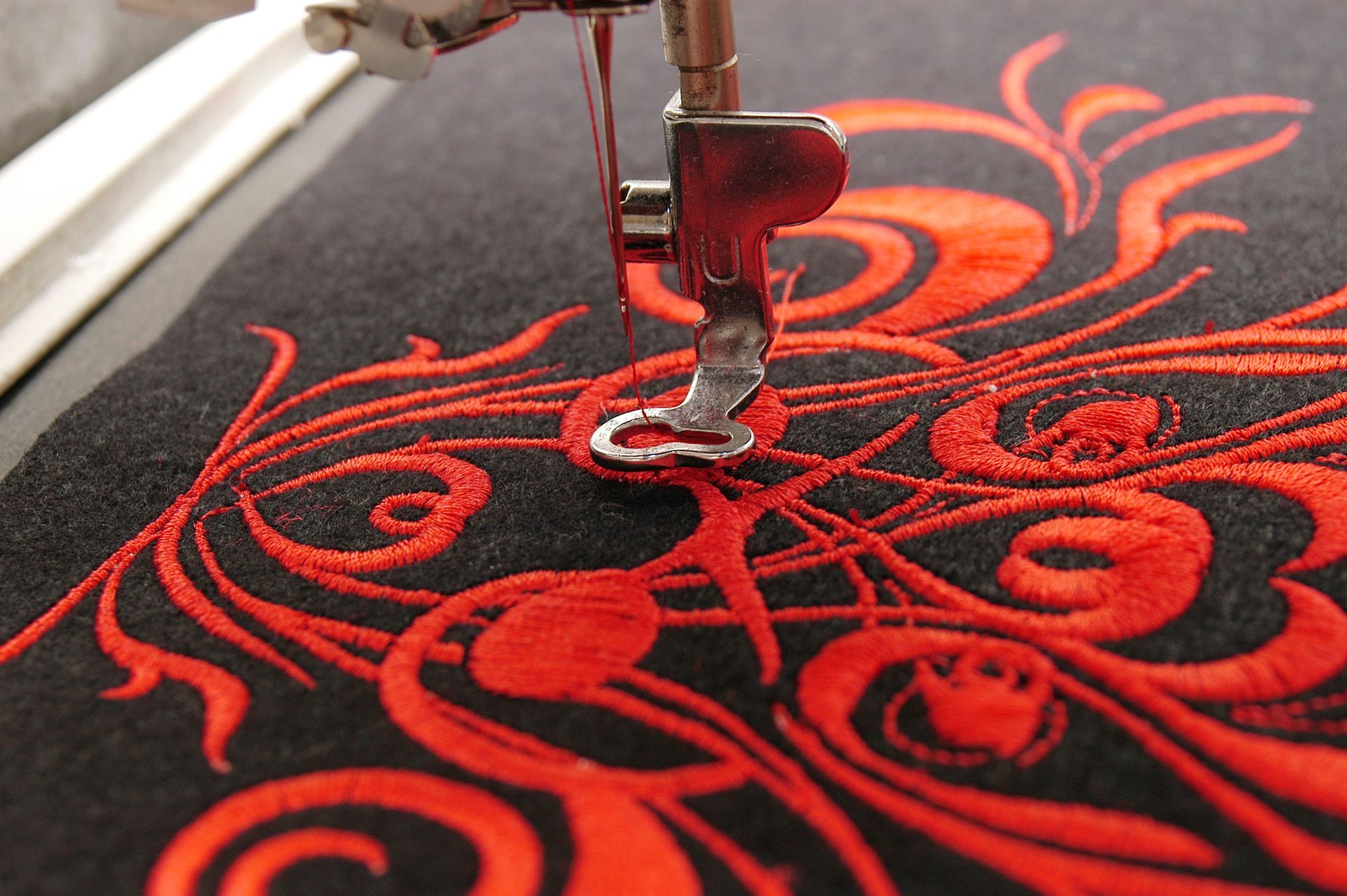 Close-up of a sewing machine stitching red thread on black fabric with a swirling floral design