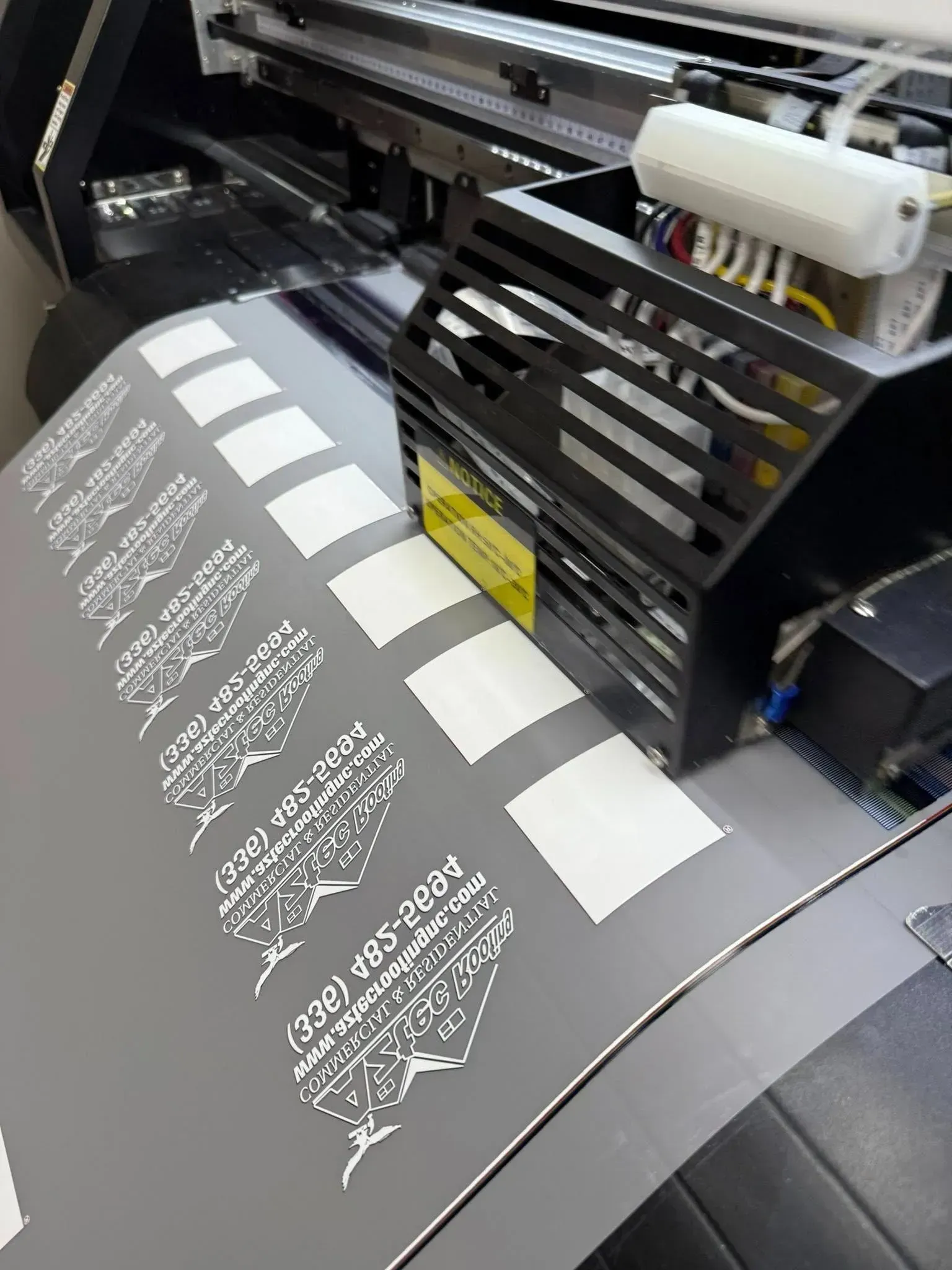 Large-format printer producing black-and-white labels on a gray sheet