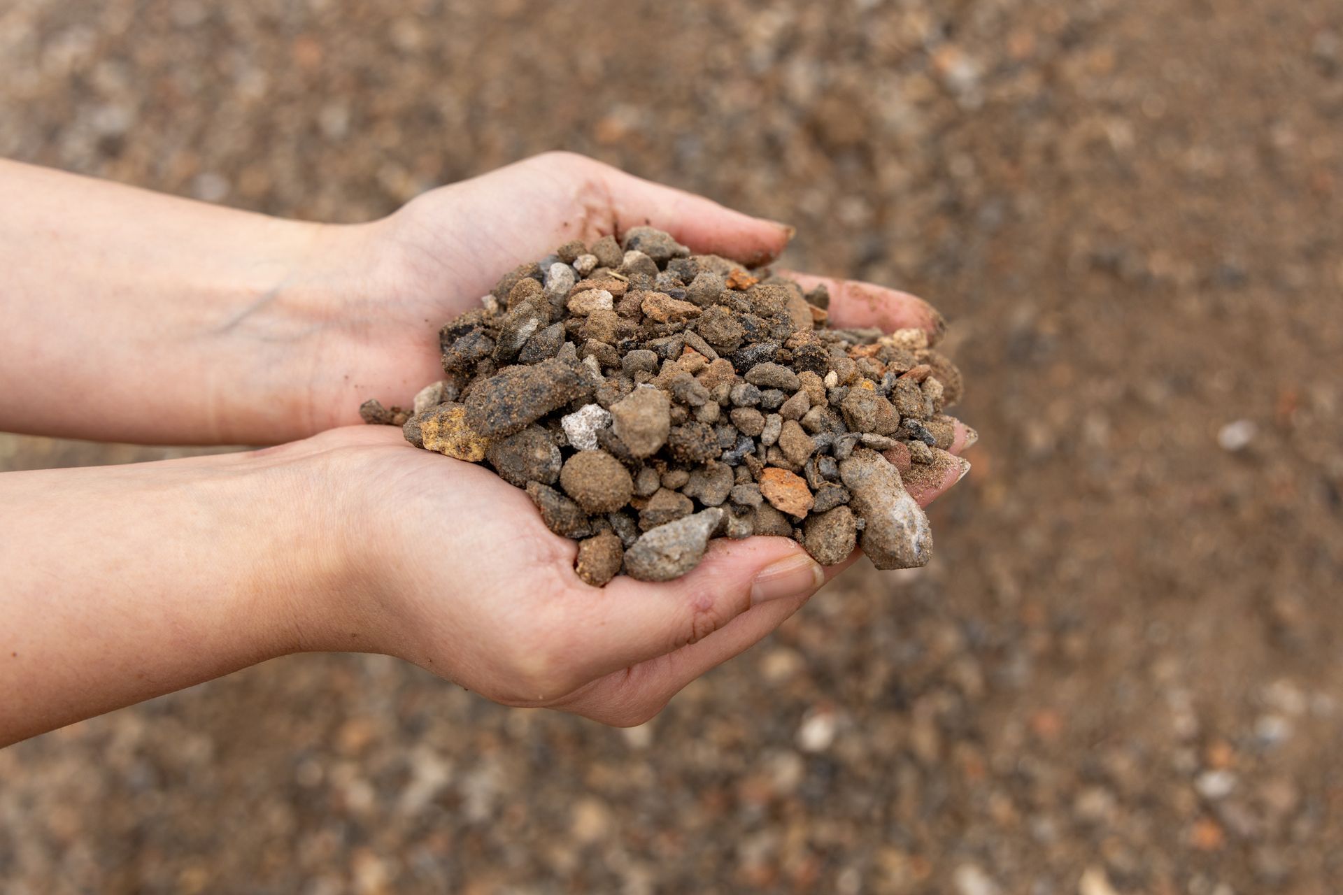 Hands Holding a Pile of Brown Gravel — Economy Waste Group | Skip Bins Central Coast In Warnervale, NSW