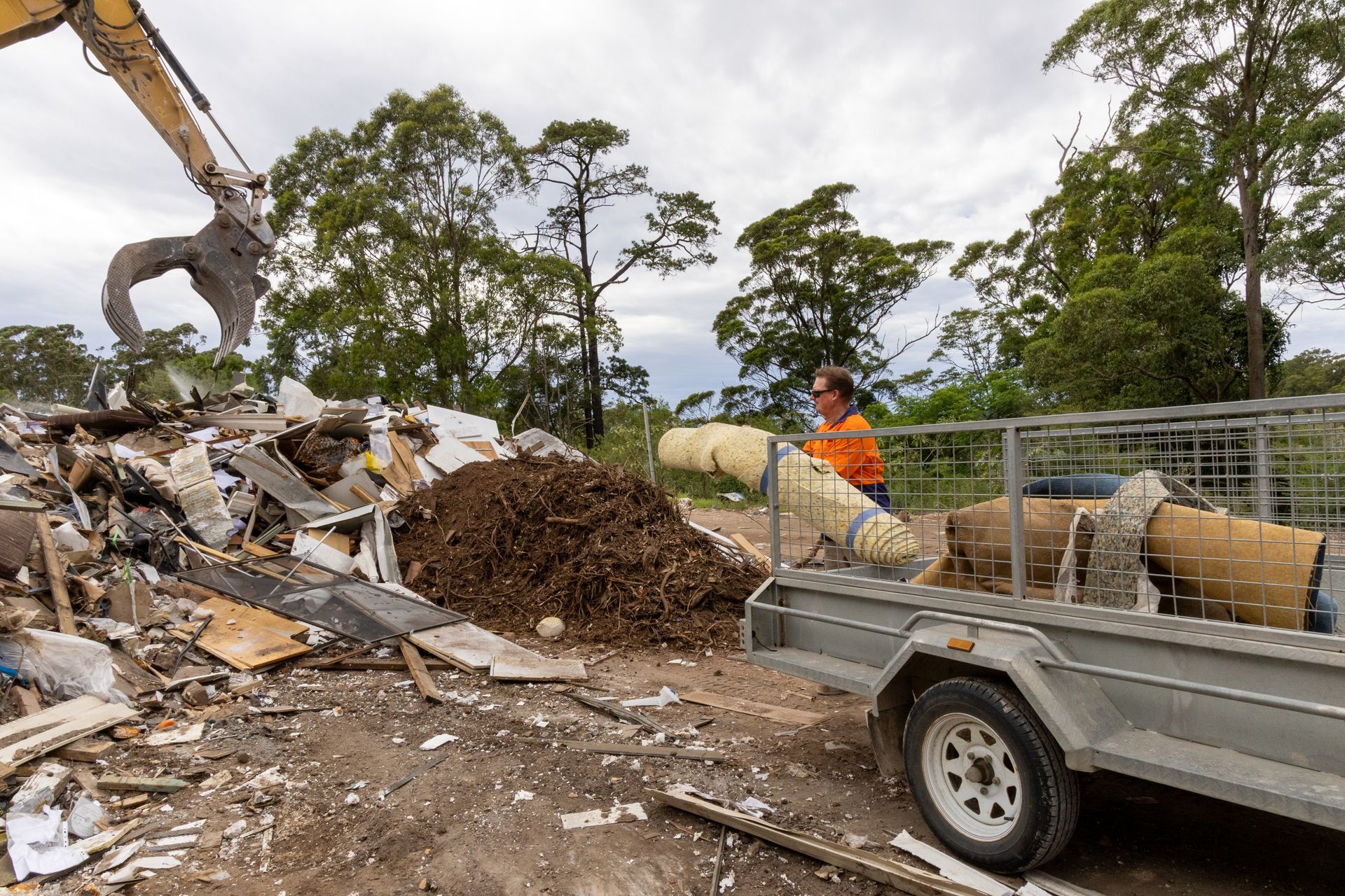 Man Loading Debris Into Trailer Near a Pile — Economy Waste Group | Skip Bins Central Coast In Lake Munmorah, NSW