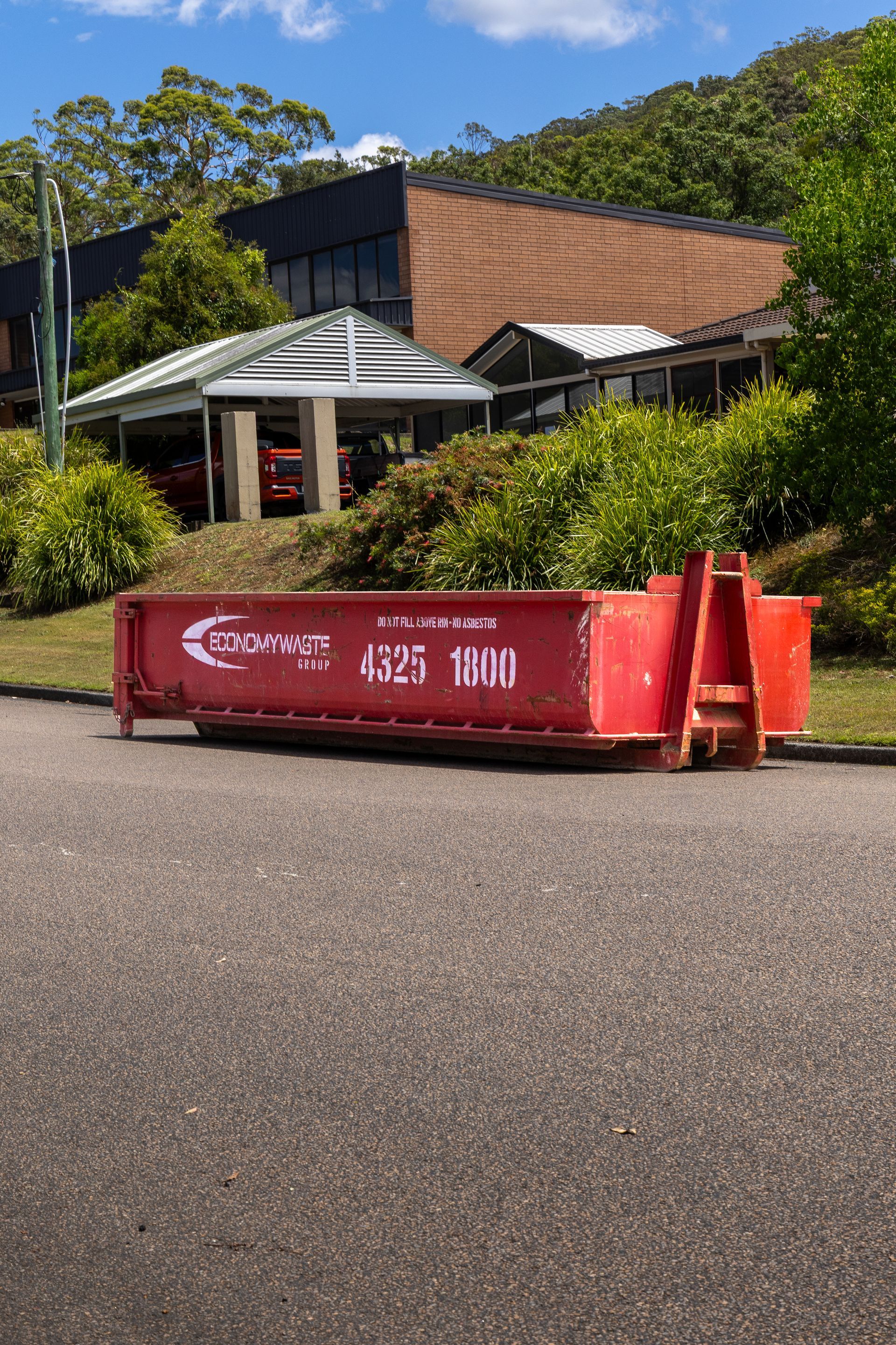 Red dumpster on asphalt road — Economy Waste Group | Skip Bins Central Coast In West Gosford, NSW