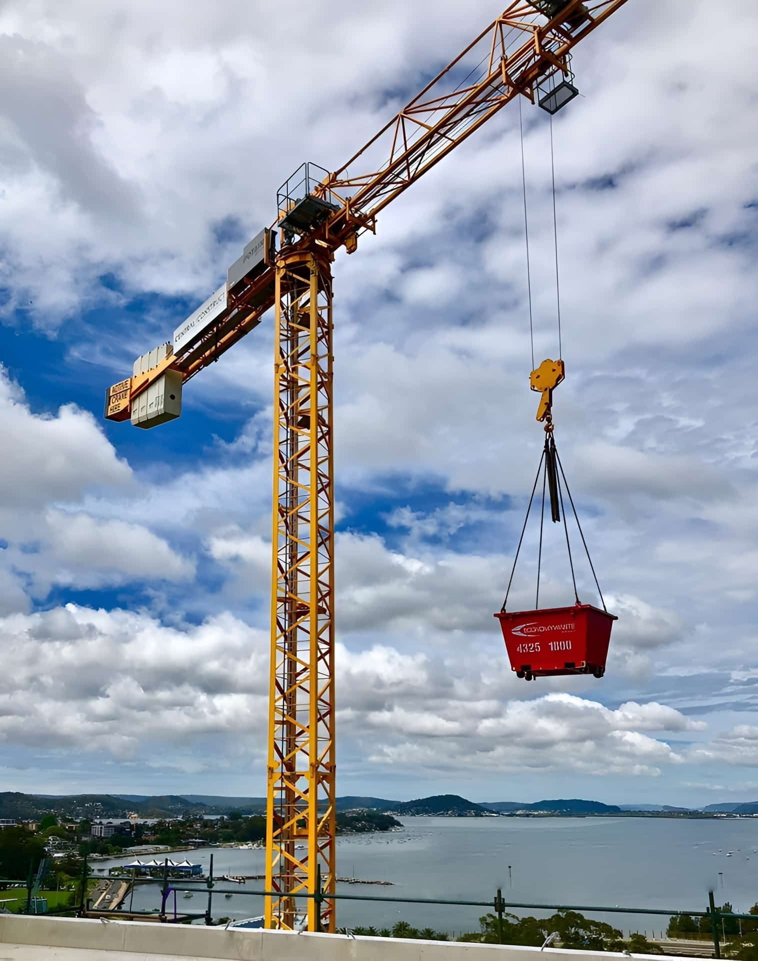 A Yellow Construction Crane Lifting a Red Bin — Economy Waste Group | Skip Bins Central Coast In Berkeley Vale, NSW